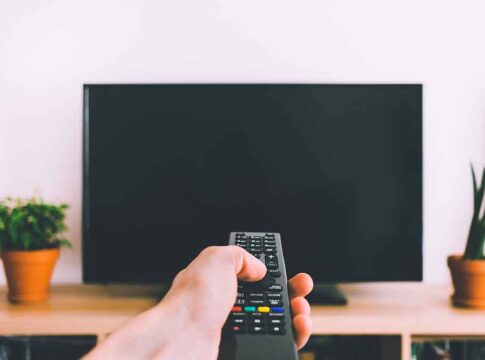 Hand holding remote towards blank TV screen.