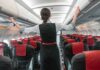 Flight attendant inspects overhead compartments in empty airplane.