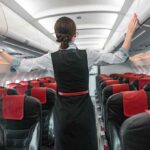 Flight attendant inspects overhead compartments in empty airplane.