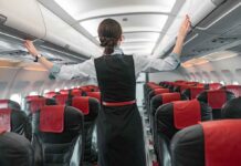 Flight attendant inspects overhead compartments in empty airplane.