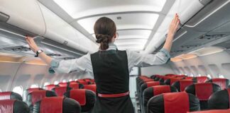 Flight attendant inspects overhead compartments in empty airplane.