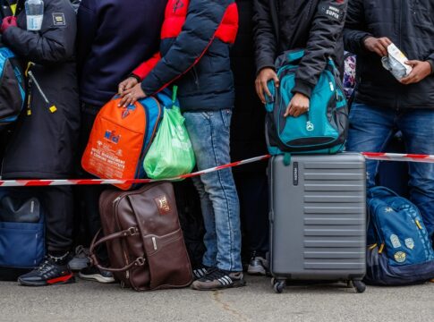 People standing with luggage behind a red and white tape.