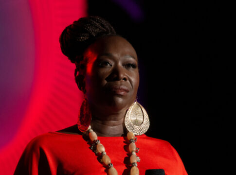 A woman speaking on stage under red lighting.