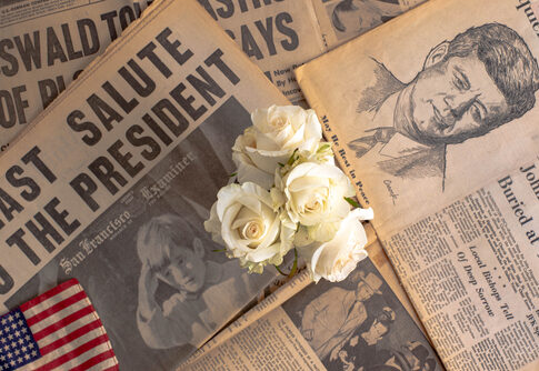 Newspapers about John F. Kennedy, white roses on top.