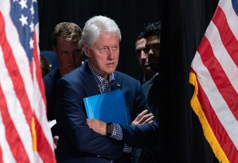 Bill Clinton standing between American flags with a folder.