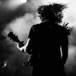 Silhouette of guitarist performing on stage with hair flying.