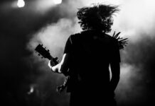 Silhouette of guitarist performing on stage with hair flying.