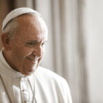 A smiling Pope Francis in white papal attire.