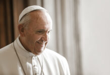 A smiling Pope Francis in white papal attire.