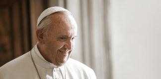 A smiling Pope Francis in white papal attire.