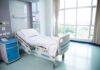 Empty hospital bed next to large window.