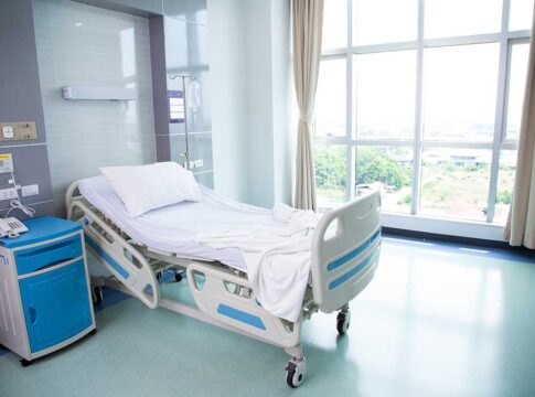 Empty hospital bed next to large window.