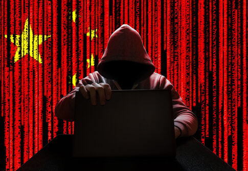 Hooded figure using laptop, China flag background with code.