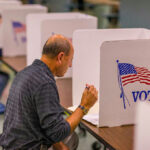 Man voting in a booth with American flag.
