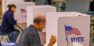 Man voting in a booth with American flag.