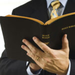 Religious Speech BANNED — Christians REVOLT… Man in suit holding an open Holy Bible.