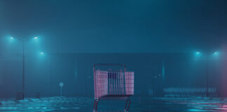 A shopping cart in an empty parking lot illuminated by neon lights in a foggy night