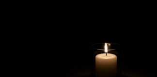 A lit candle in a glass holder against a dark background
