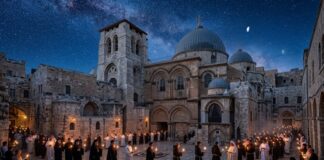 A group of people holding candles in a historic courtyard under a starry sky