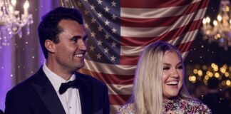 A smiling couple in formal attire standing in front of an American flag backdrop