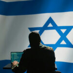 Sabotage From Within? Israel Attack Plans EXPOSED… Hacker in front of Israeli flag with laptop.