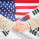 Handshake between two individuals with American and South Korean flags in the background