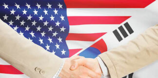 Handshake between two individuals with American and South Korean flags in the background