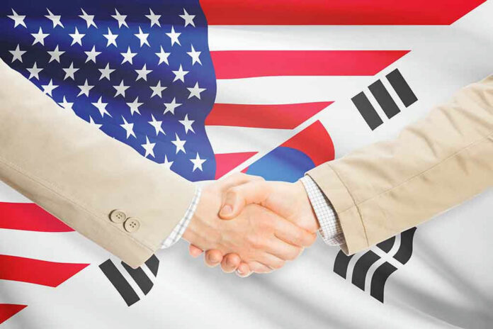 Handshake between two individuals with American and South Korean flags in the background