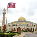 A mosque with a golden dome and minarets, featuring an American flag in front