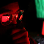 Marxist Billionaire’s SHOCKING Propaganda Machine Exposed… Person wearing glasses with a reflection of the Chinese flag, surrounded by computer screens