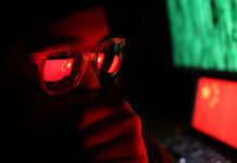 Marxist Billionaire’s SHOCKING Propaganda Machine Exposed… Person wearing glasses with a reflection of the Chinese flag, surrounded by computer screens
