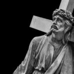 A black and white statue of Christ carrying a cross with a sorrowful expression