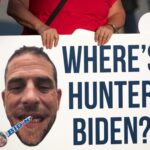A protestor holding a sign with a large image of a mans face and the text WHERES HUNTER BIDEN?