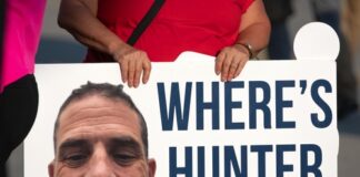 A protestor holding a sign with a large image of a mans face and the text WHERES HUNTER BIDEN?