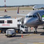 An airplane at an airport with an ambulance and ground crew nearby