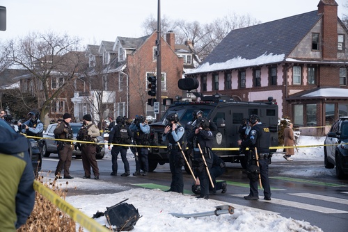 Police officers at a crime scene with a tactical vehicle in a snowy urban area