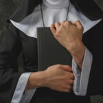 A nun in traditional attire holding a book close to her chest