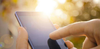 Finger touching smartphone screen with sunlight background.