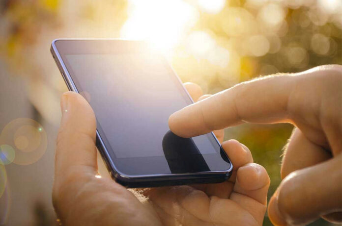 Finger touching smartphone screen with sunlight background.