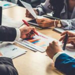 Billionaire Blackmail List Leaks People discussing charts and graphs at a meeting.