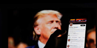 Hand holding smartphone displaying Twitter profile.