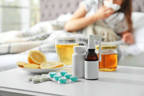 Medicines, honey, and lemon on table beside sick person.