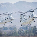 Two military helicopters flying near mountains.
