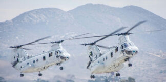 Two military helicopters flying near mountains.