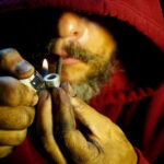 Tobacco Giant’s ‘Efficiency’ Bloodbath Person igniting a pipe, wearing a red hoodie.
