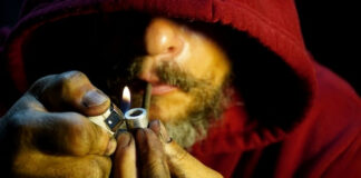 Person igniting a pipe, wearing a red hoodie.