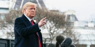 A man in a suit gesturing while speaking at a press conference outside the White House