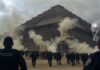 Crowd of people running near a pyramid with police officers observing