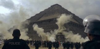Crowd of people running near a pyramid with police officers observing