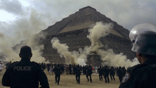 Crowd of people running near a pyramid with police officers observing